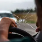 汽车挡风玻璃碎了。三层挡风玻璃上有放射状的裂缝。破损的汽车挡风玻璃，损坏的玻璃，路上有迎面而来的石头痕迹或汽车玻璃上的子弹痕迹